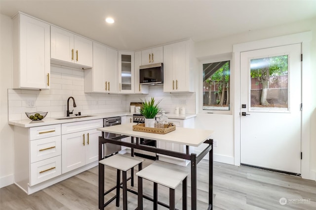 kitchen featuring stainless steel appliances, a sink, white cabinets, light countertops, and glass insert cabinets