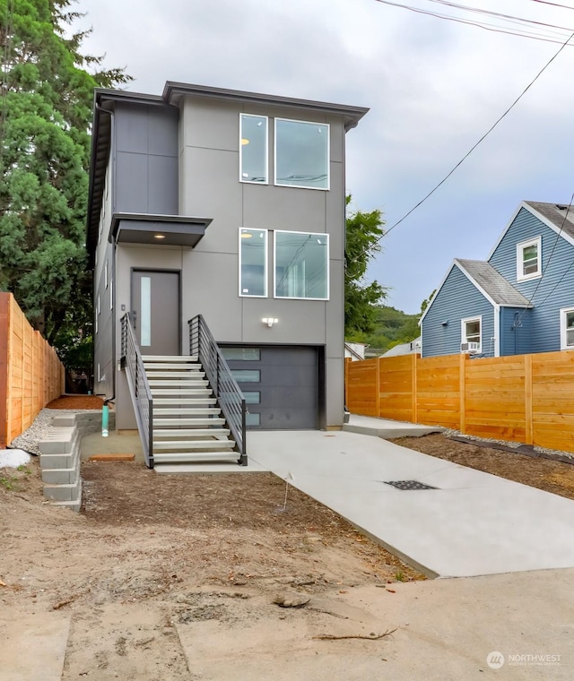 contemporary house featuring a garage, fence, stairs, concrete driveway, and stucco siding