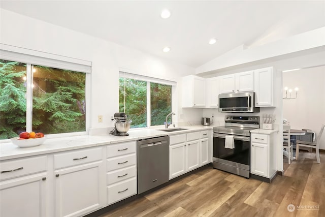 kitchen featuring white cabinets, vaulted ceiling, appliances with stainless steel finishes, light hardwood / wood-style floors, and sink