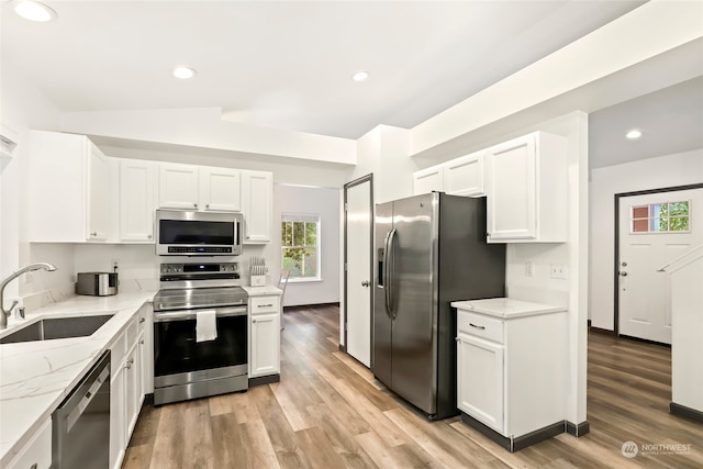 kitchen with light hardwood / wood-style flooring, appliances with stainless steel finishes, light stone counters, sink, and lofted ceiling