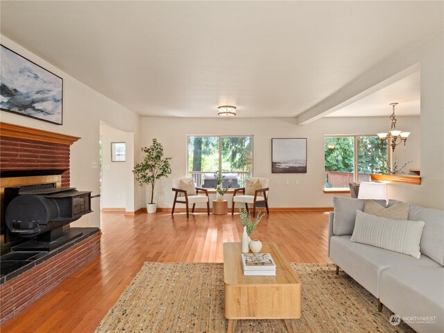 living room featuring beamed ceiling, a chandelier, hardwood / wood-style flooring, and a brick fireplace