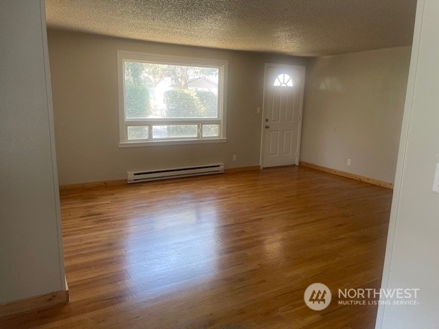 spare room with a baseboard radiator, light hardwood / wood-style floors, and a textured ceiling