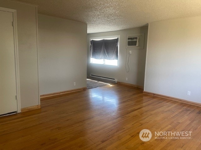 unfurnished room featuring a baseboard radiator, light hardwood / wood-style floors, a textured ceiling, and a wall unit AC