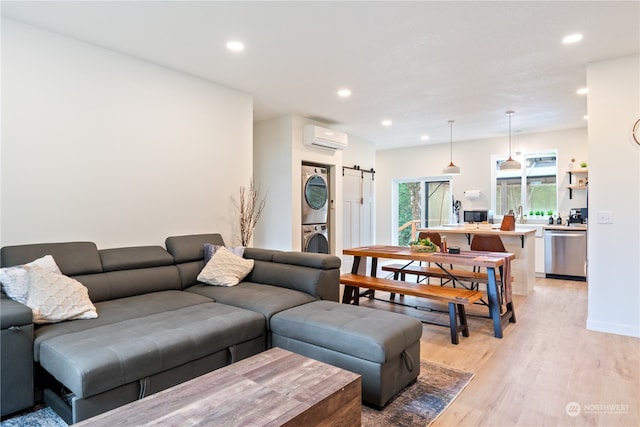 living room with stacked washing maching and dryer, a barn door, light hardwood / wood-style flooring, and a wall mounted AC