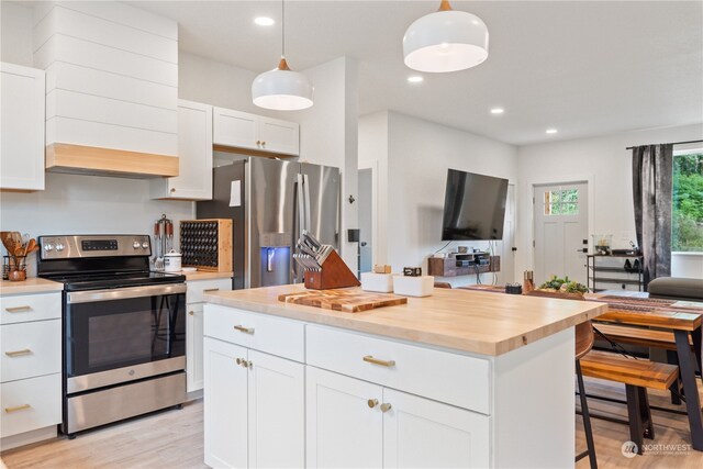 kitchen with light wood-type flooring, white cabinets, appliances with stainless steel finishes, butcher block counters, and a center island