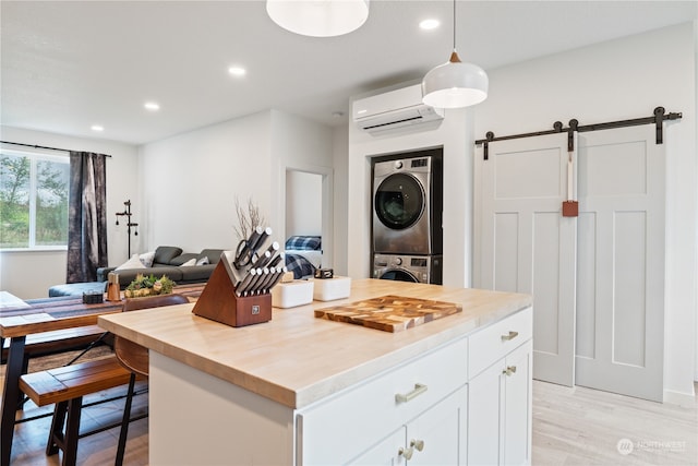 kitchen with stacked washing maching and dryer, light hardwood / wood-style flooring, white cabinets, a barn door, and a wall unit AC