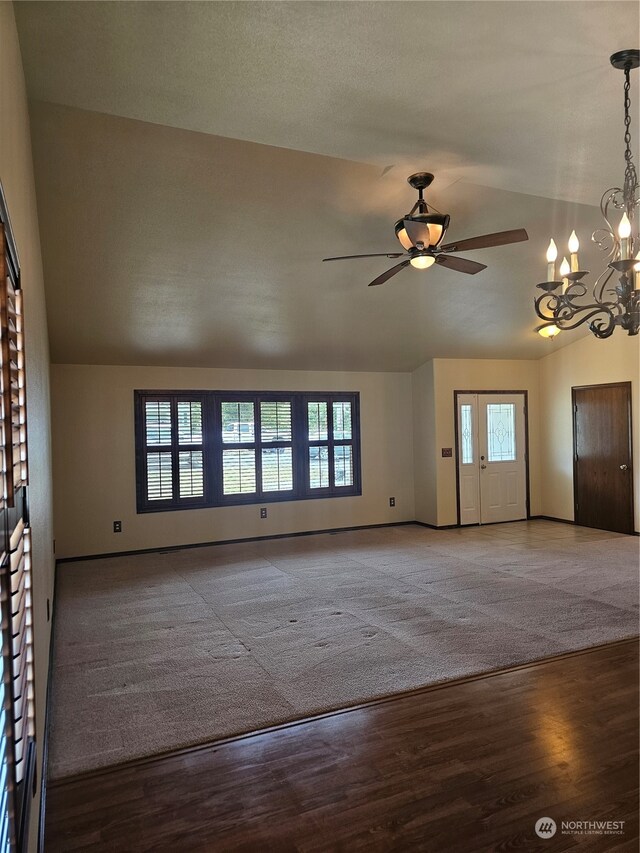 unfurnished living room featuring carpet flooring, vaulted ceiling, ceiling fan with notable chandelier, and a healthy amount of sunlight