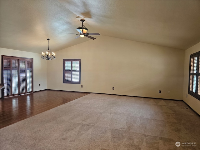 carpeted empty room with plenty of natural light, ceiling fan with notable chandelier, and lofted ceiling