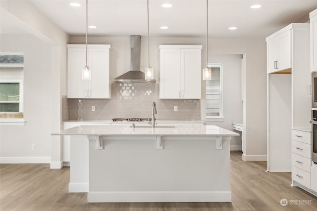 kitchen featuring white cabinetry, a kitchen island with sink, wall chimney exhaust hood, and pendant lighting