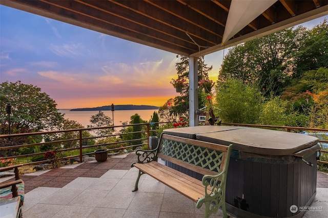 patio terrace at dusk with a water view and a hot tub