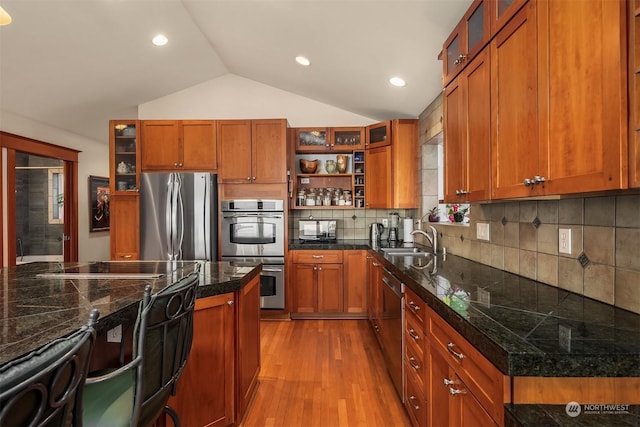 kitchen featuring appliances with stainless steel finishes, decorative backsplash, light hardwood / wood-style floors, vaulted ceiling, and sink