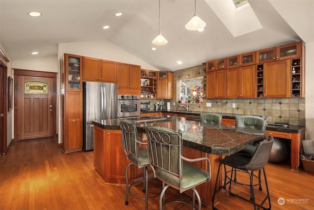 kitchen with a center island, decorative light fixtures, lofted ceiling with skylight, appliances with stainless steel finishes, and a kitchen breakfast bar