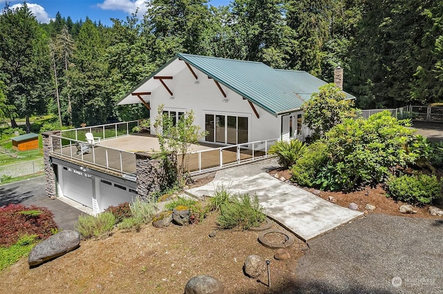 view of front of home with aphalt driveway, a chimney, an attached garage, a standing seam roof, and metal roof