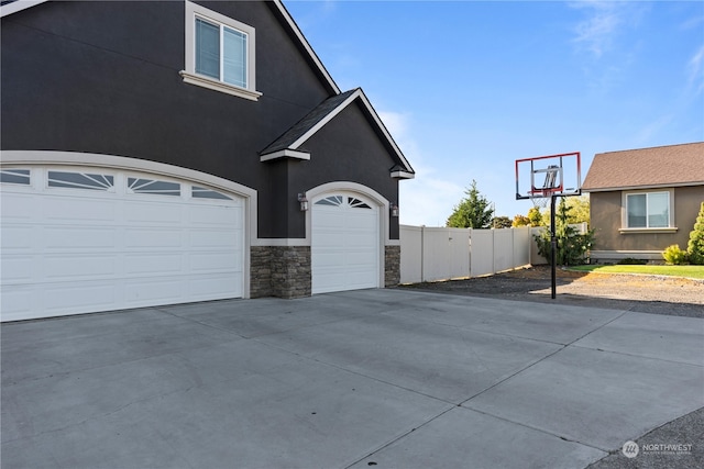 view of property exterior with stone siding, driveway, fence, and stucco siding