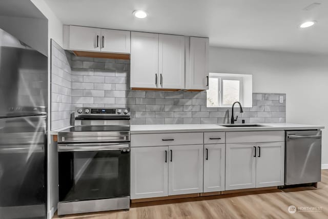 kitchen featuring backsplash, sink, appliances with stainless steel finishes, light hardwood / wood-style flooring, and white cabinets