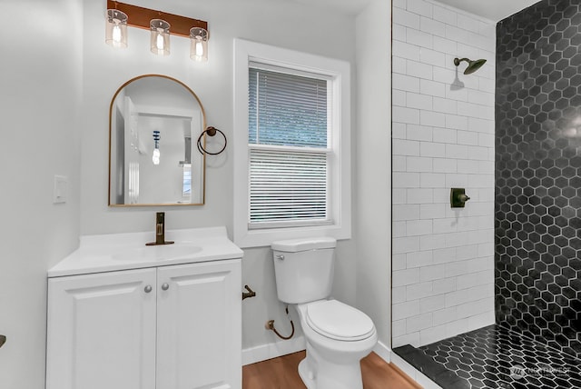 bathroom featuring toilet, hardwood / wood-style floors, vanity, and a tile shower