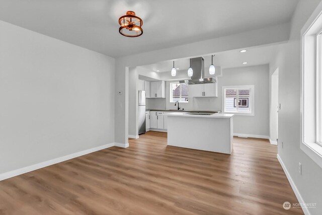 kitchen with ventilation hood, white cabinetry, light hardwood / wood-style floors, decorative light fixtures, and stainless steel fridge