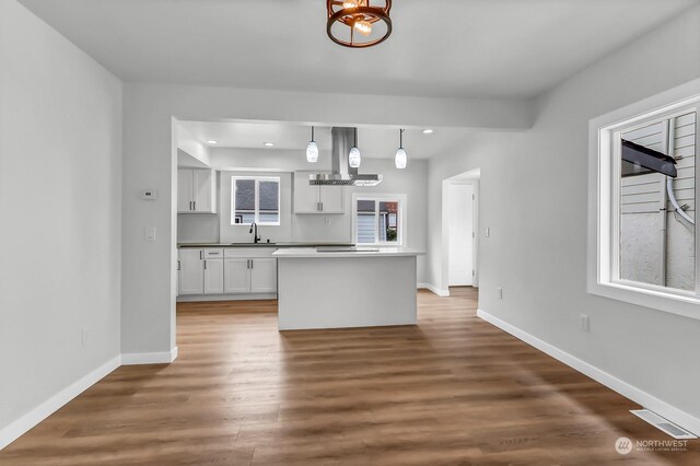 kitchen featuring decorative light fixtures, hardwood / wood-style floors, white cabinetry, sink, and island exhaust hood