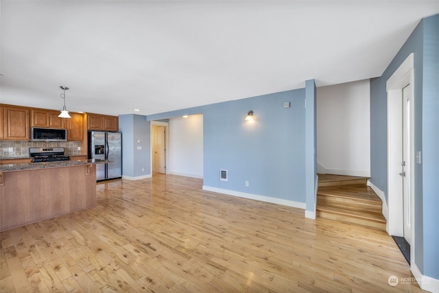 kitchen with appliances with stainless steel finishes, light hardwood / wood-style flooring, decorative light fixtures, decorative backsplash, and dark stone counters