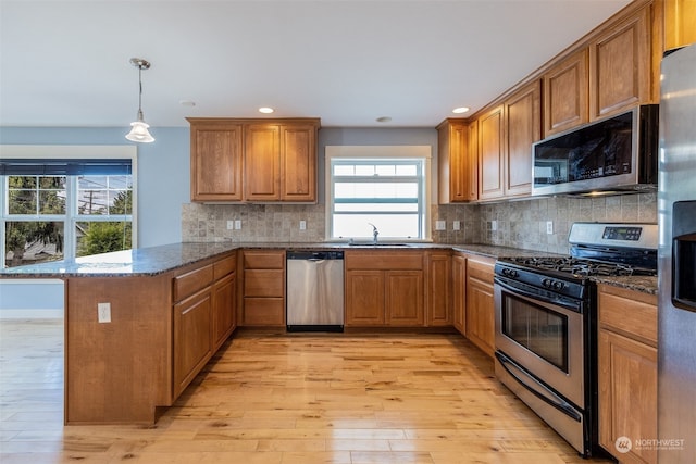 kitchen featuring tasteful backsplash, kitchen peninsula, light hardwood / wood-style floors, and stainless steel appliances