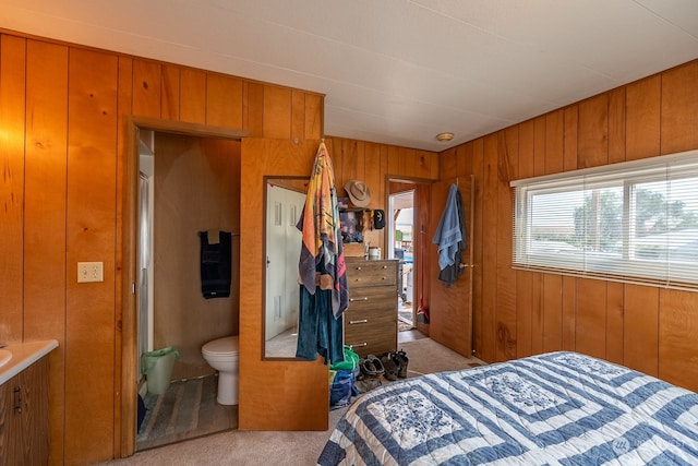 carpeted bedroom with wood walls and connected bathroom