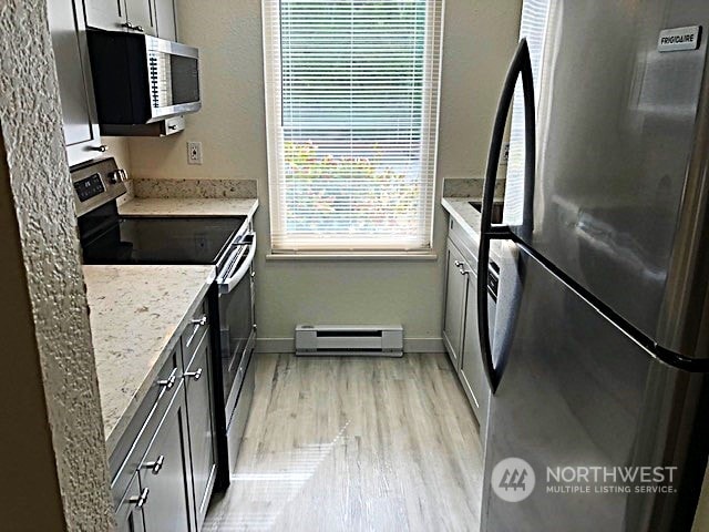 12602 NE 118th St, Kirkland, WA 98034 - kitchen with a baseboard heating unit, light wood-type flooring, baseboards, light stone countertops, and appliances with stainless steel finishes