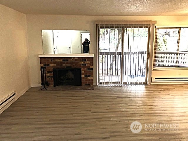 12602 NE 118th St, Kirkland, WA 98034 - unfurnished living room featuring a fireplace, wood finished floors, baseboard heating, and a textured ceiling