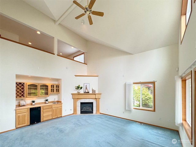 unfurnished living room featuring beamed ceiling, a tiled fireplace, high vaulted ceiling, carpet flooring, and ceiling fan