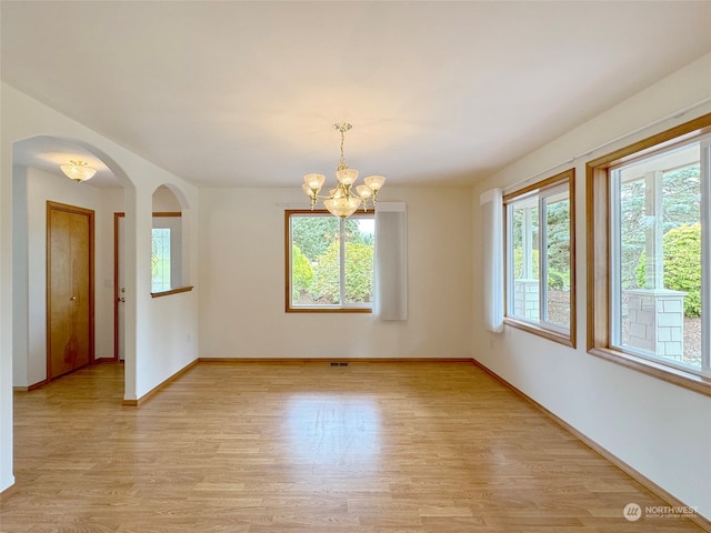 unfurnished room featuring a notable chandelier, light hardwood / wood-style floors, and a healthy amount of sunlight