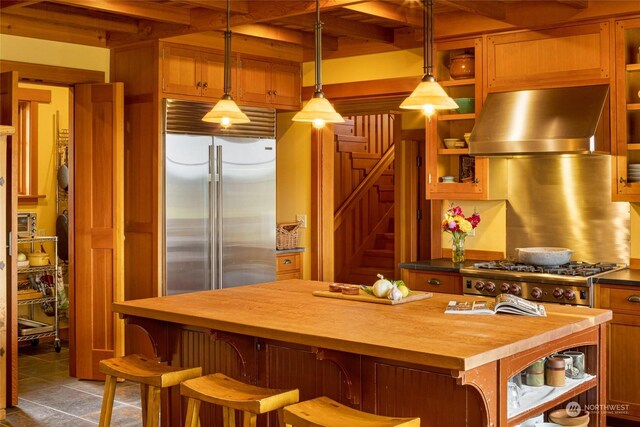 kitchen featuring pendant lighting, tile patterned flooring, built in refrigerator, a kitchen bar, and wall chimney range hood