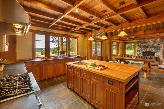 kitchen featuring beamed ceiling, butcher block counters, exhaust hood, a center island, and a stone fireplace