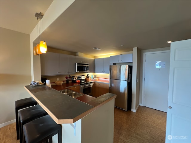 kitchen with sink, a breakfast bar area, stainless steel appliances, kitchen peninsula, and pendant lighting