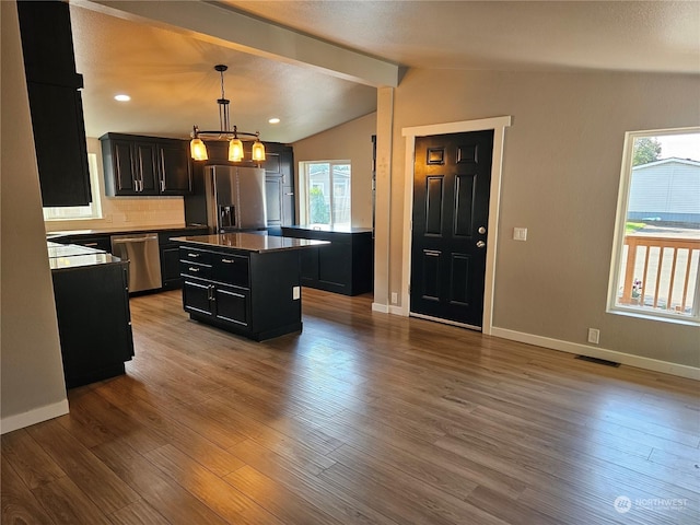 kitchen with pendant lighting, vaulted ceiling with beams, light wood finished floors, appliances with stainless steel finishes, and a kitchen island