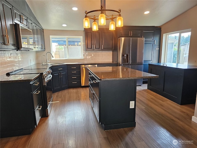 kitchen featuring light wood-style flooring, decorative light fixtures, a center island, stainless steel appliances, and a sink