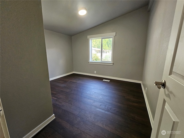 spare room featuring dark wood-type flooring and vaulted ceiling