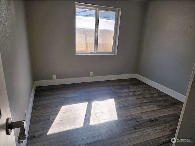 spare room with baseboards and dark wood-style flooring