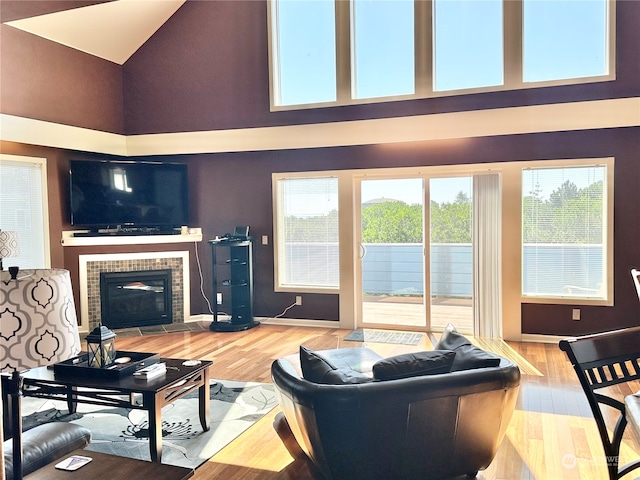 living room featuring a tiled fireplace, a towering ceiling, and hardwood / wood-style floors