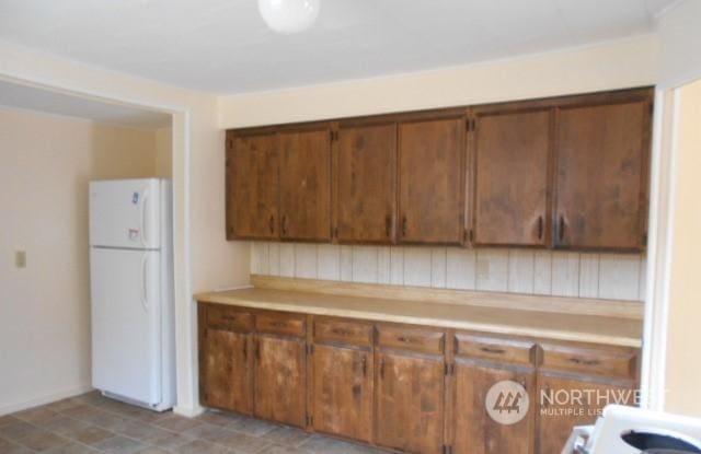 kitchen featuring light countertops, freestanding refrigerator, and brown cabinets