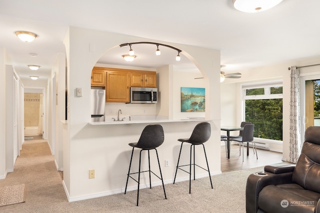 kitchen with ceiling fan, light colored carpet, a kitchen bar, appliances with stainless steel finishes, and sink