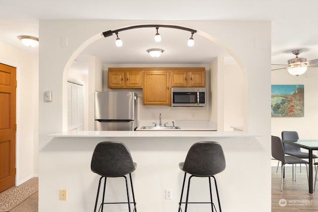 kitchen with appliances with stainless steel finishes, rail lighting, sink, a breakfast bar area, and ceiling fan