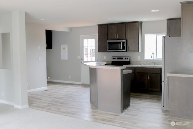 kitchen with a kitchen island, dark brown cabinets, appliances with stainless steel finishes, sink, and light wood-type flooring