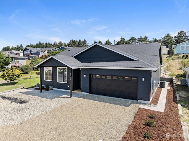 view of front of property featuring a shingled roof, an attached garage, cooling unit, and gravel driveway