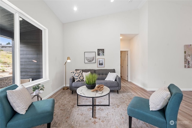 living room with high vaulted ceiling, light wood-type flooring, and baseboards