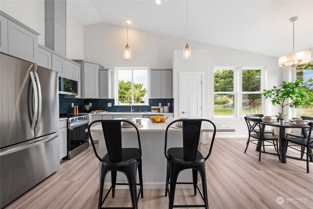 kitchen featuring appliances with stainless steel finishes, hanging light fixtures, light hardwood / wood-style flooring, and backsplash