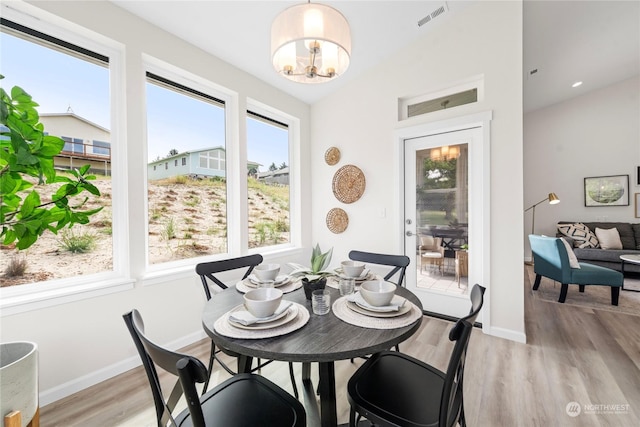 dining area featuring a notable chandelier, light wood finished floors, visible vents, vaulted ceiling, and baseboards