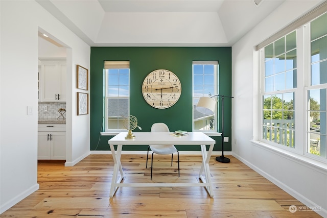 home office featuring light wood-type flooring and a tray ceiling