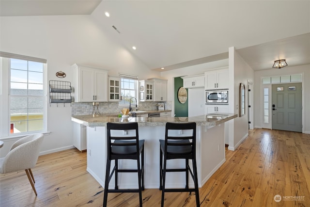 kitchen featuring white cabinetry, stainless steel microwave, light stone counters, and light hardwood / wood-style flooring