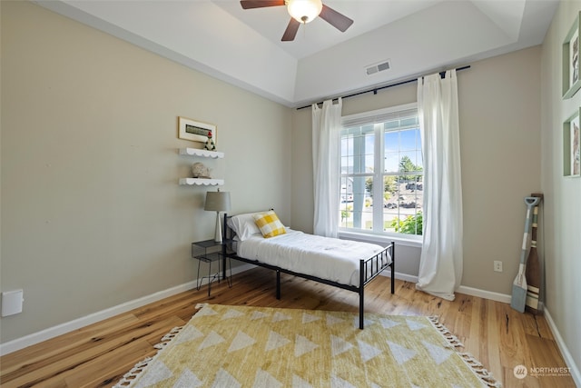 bedroom with a raised ceiling, ceiling fan, and light hardwood / wood-style floors