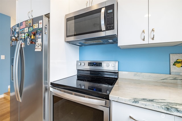 kitchen with light stone counters, white cabinetry, stainless steel appliances, and hardwood / wood-style flooring