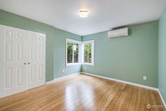 unfurnished bedroom with an AC wall unit, light hardwood / wood-style flooring, and a closet